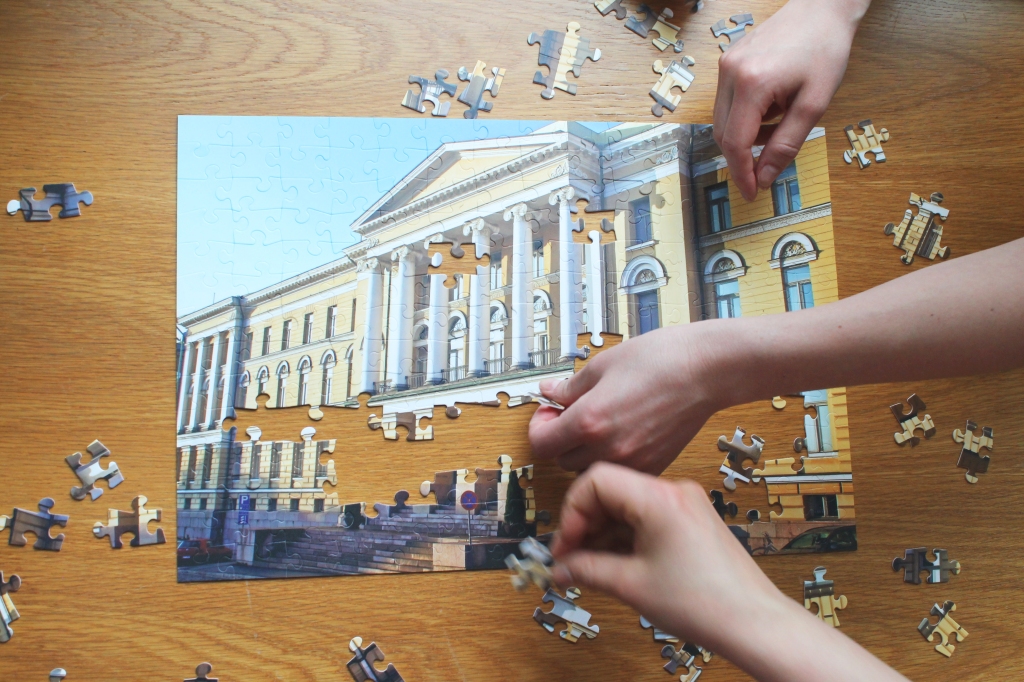 Hands laying a puzzle with a picture of the University of Helsinki Main building. 